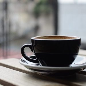 selective focus photography of black ceramic tea mug and plate on brown wooden table during daytime