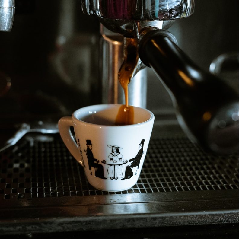white and black ceramic mug on black and silver coffee maker