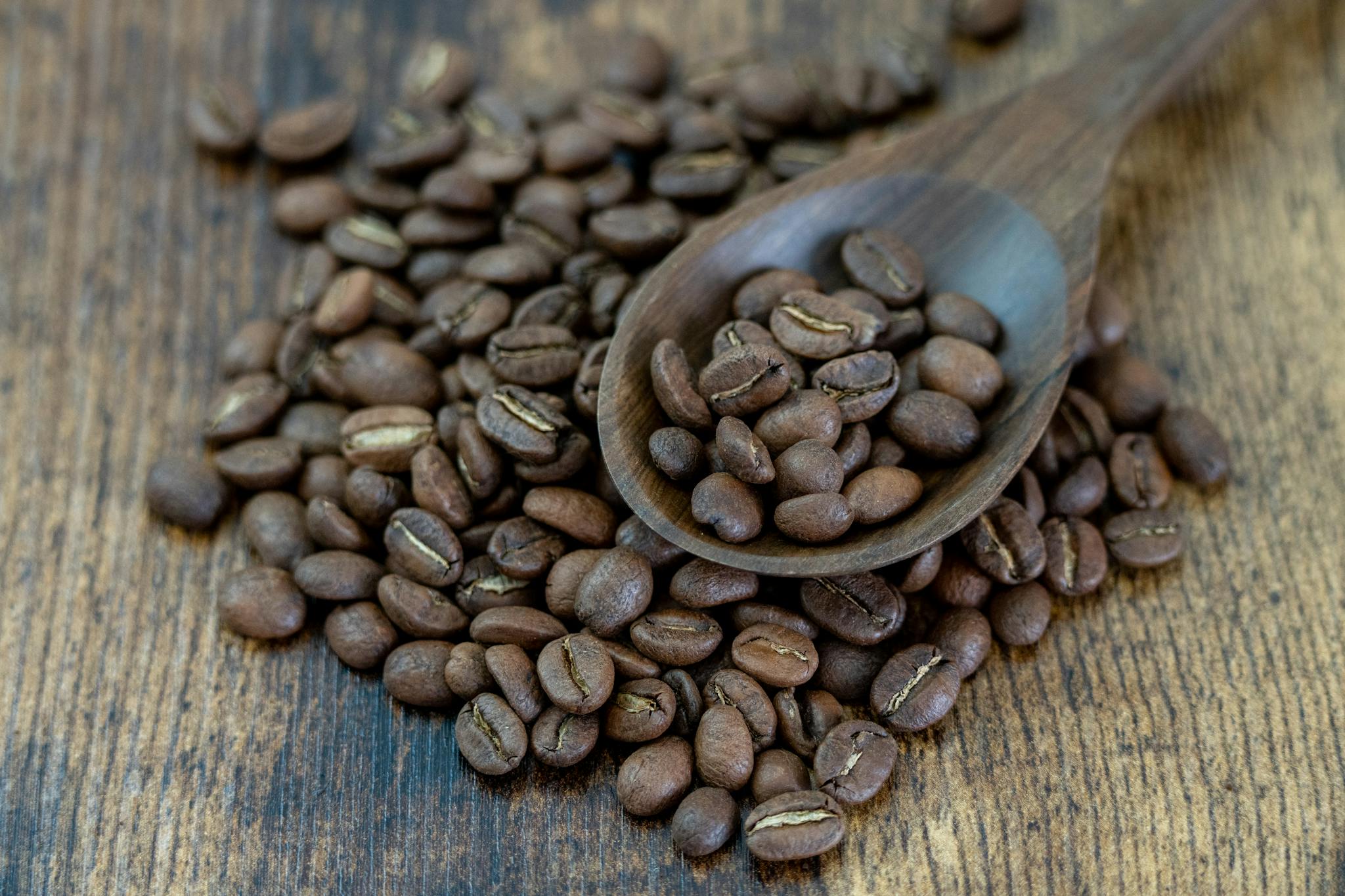 Close-up of Colombian coffee beans with a wooden spoon on a rustic surface, highlighting rich texture and color.